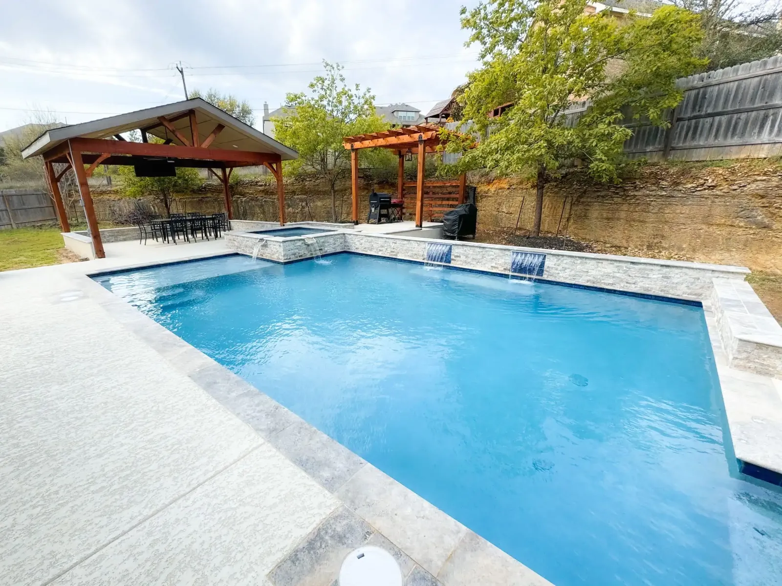 Pool with a wide light stone deck and a covered pavilion
